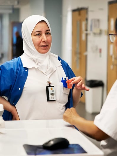 En kvinna i vita arbetskläder pratar med en kvinnlig kollega en korridor.