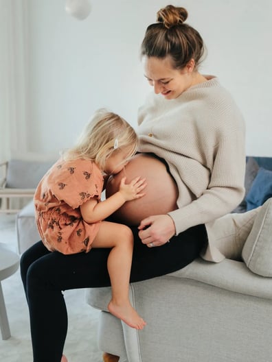 En liten flicka sitter i en gravid kvinnas knä.