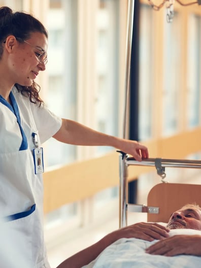 En sjuksköterska skjutsar en patient i en sjukhussäng i en sjukhuskorridor.