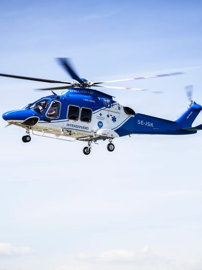 En blå och vit helikopter som flyger på himlen.