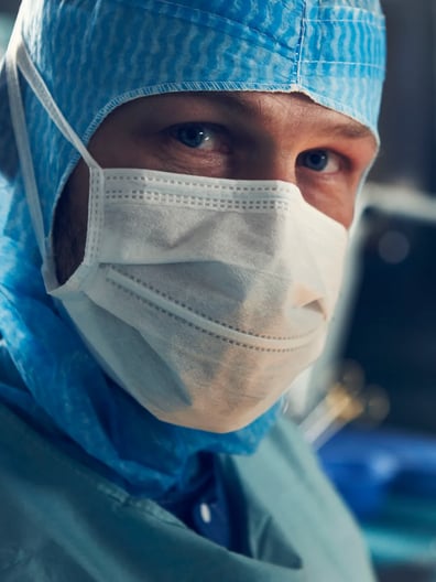 En kirurg iförd kirurgmask och operationskläder.