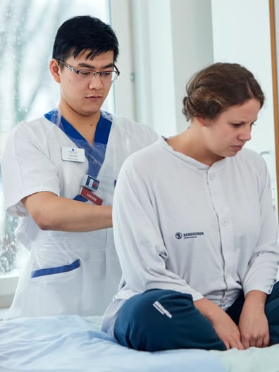 En man i vårdkläder undersöker en patient som sitter på en sjukhussäng.