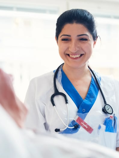 En kvinna i vit rock med stetoskop ler mot patient.