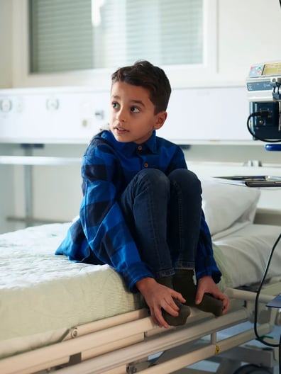 En ung pojke sitter på en sjukhussäng.