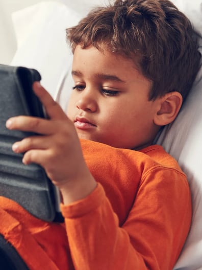 En ung pojke ligger i en sjukhussäng och tittar på en surfplatta.