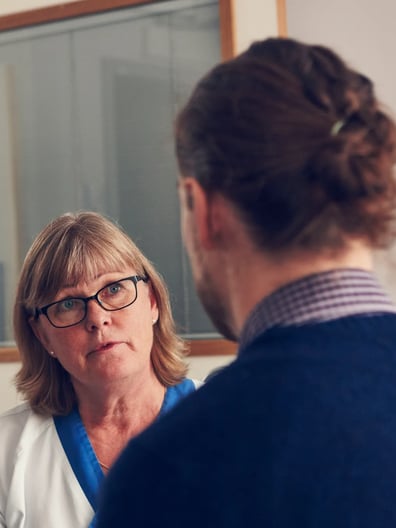 En kvinna i vårdkläder pratar med en patient.