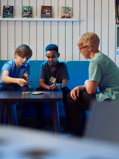 Två pojkar spelar kort med en vuxen i ett tonårsrum.