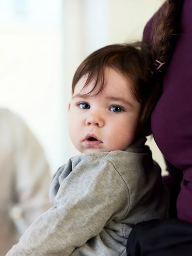 En mamma håller i sitt barn i famnen som tittar in i kameran.