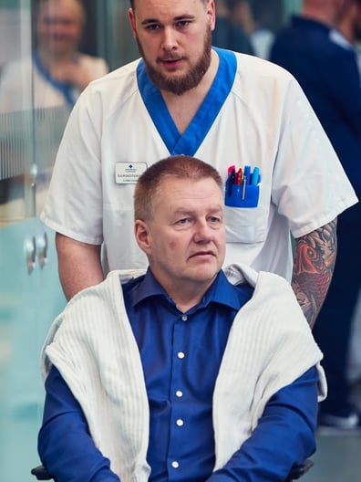 En sjuksköterska skjutsar en man i rullstol.