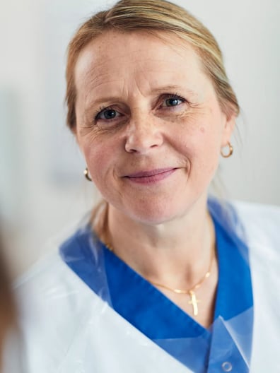 En kvinna i vit labbrock ler mot kameran.