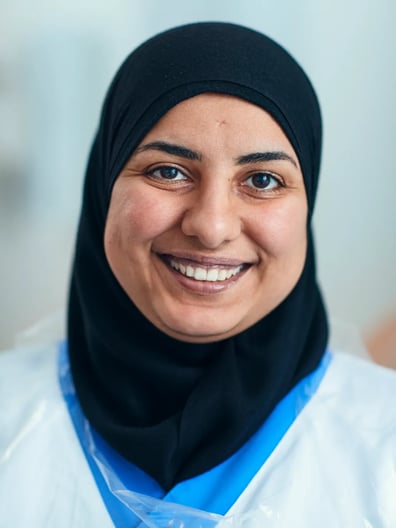 En kvinna i hijab som jobbar inom vården ler mot kameran.