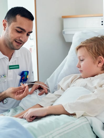 En liten pojke i en sjukhussäng undersöks av en läkare.