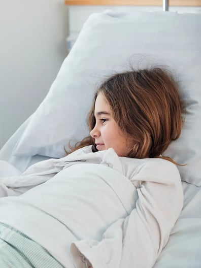 En liten flicka som ligger i en sjukhussäng.