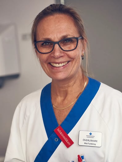 En kvinna i vita vårdkläder ler mot kameran.