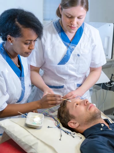 En man som ligger i en sjukhussäng och undersöks av vårdpersonal.