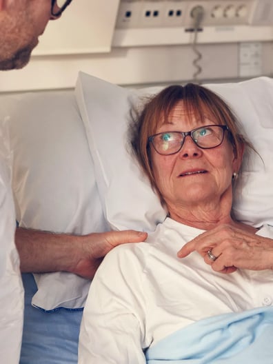 En äldre kvinna i en sjukhussäng pratar med en läkare.