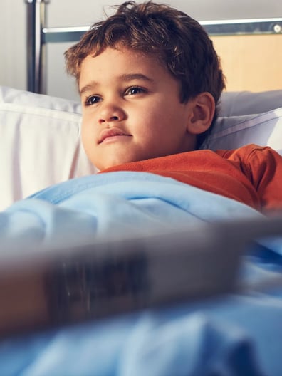 En ung pojke ligger i en sjukhussäng.