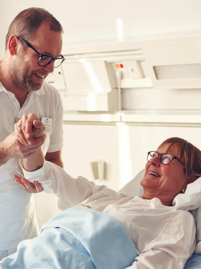 En patient i en sjukhussäng ler mot en läkare.