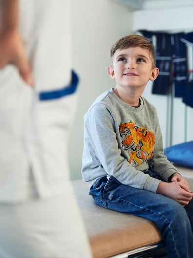 En ung pojke sitter på en sjukhussäng.