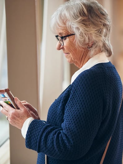En äldre kvinna tittar på sin mobiltelefon i en sjukhuskorridor.