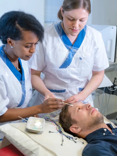 En man som ligger i en sjukhussäng och undersöks av två neurologer.