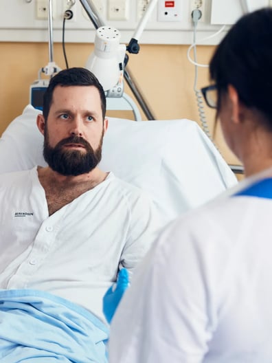 En patient som sitter i en sjukhussäng pratar med en läkare.