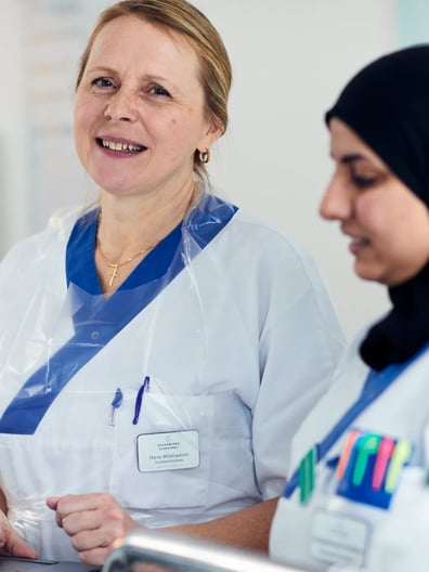 Två kvinnor i vårdkläder ler.