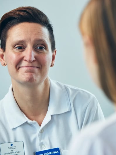 En sjuksköterska pratar med en patient i vit tröja.