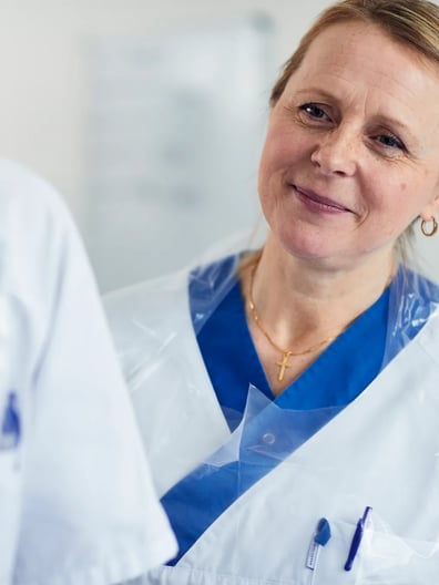 En kvinna i vit labbrock pratar med en annan kvinna.