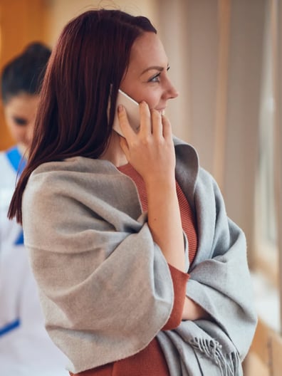 En kvinna pratar i mobiltelefon medan hon står bredvid ett fönster.