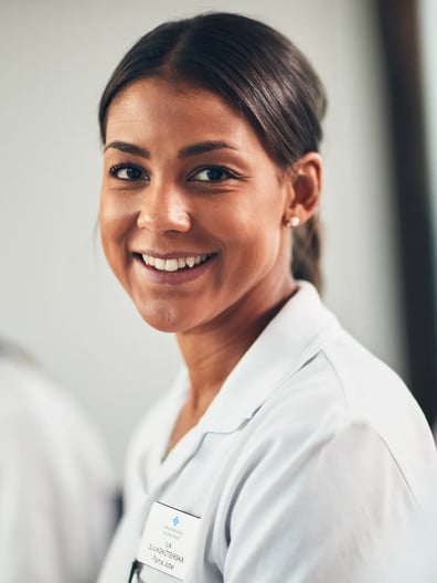 En kvinna i vit labbrock ler mot kameran.