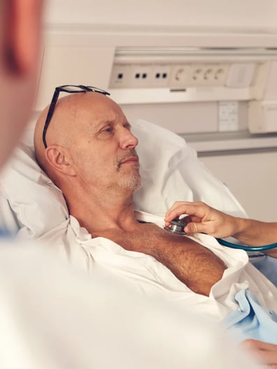 En man i en sjukhussäng undersöks av en sjuksköterska.