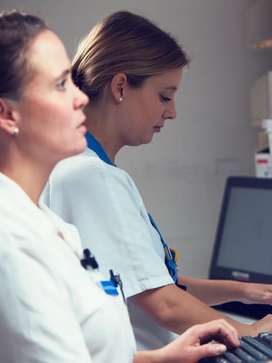 Två kvinnor arbetar vid en dator i ett läkemedelsförråd.