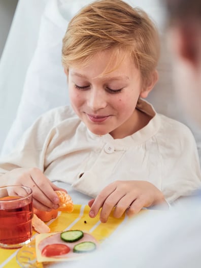 En liten pojke sitter i en sjukhussäng med en bricka med mat.
