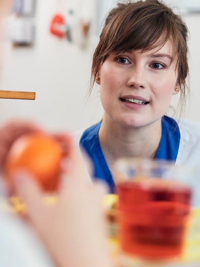 En dietist pratar med en patient som äter en apelsin och dricker saft.