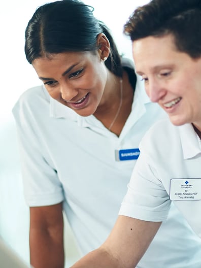 Två kvinnor i vita skjortor tittar på en surfplatta.