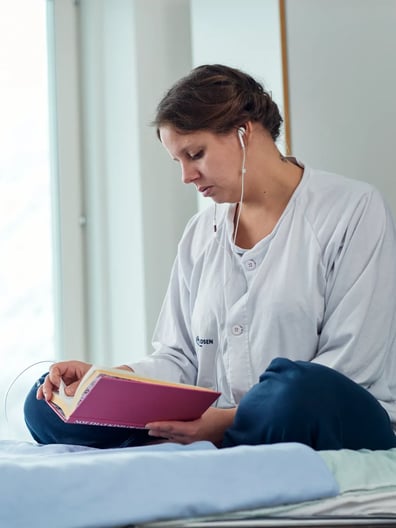 En patient sitter på en sjukhussäng och läser en bok.