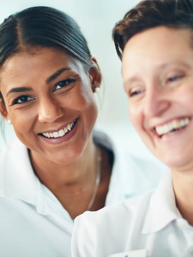 Två kvinnor och ler medan de tittar på en bärbar dator.