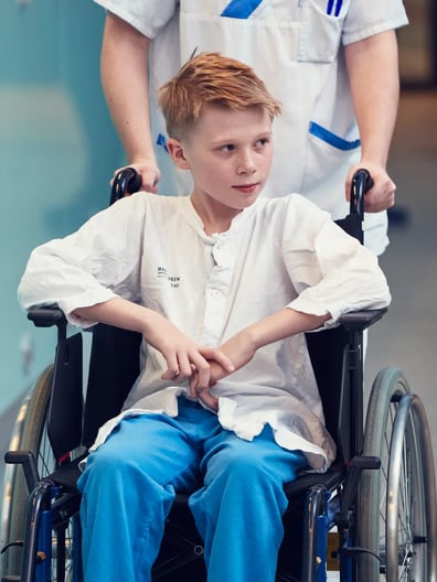 En pojke i rullstol skjutsas av en sjuksköterska.