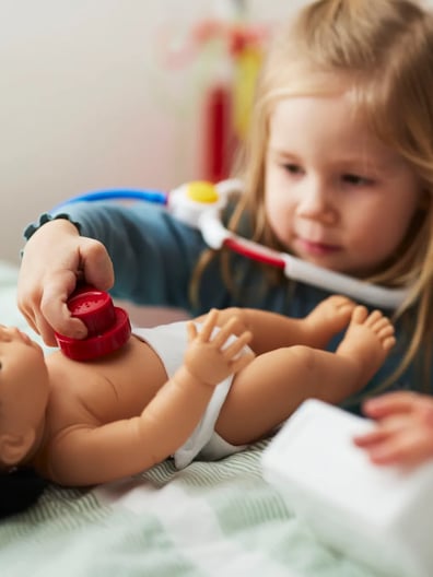 En liten flicka leker med en docka på en säng.