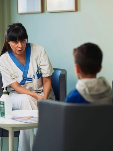 En logoped och en pojke sitter i fåtöljer mitt emot varandra och pratar.