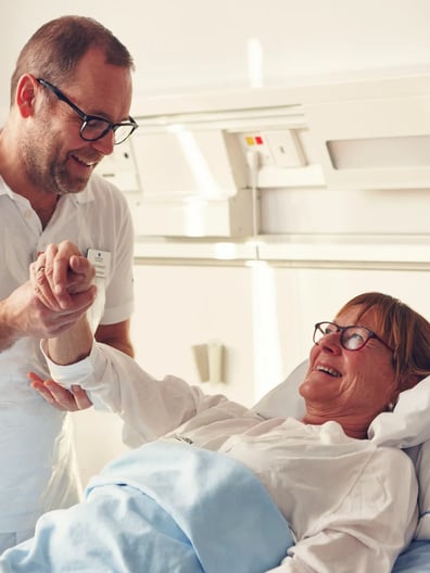 En patient i en sjukhussäng får hjälp av en sjuksköterska.