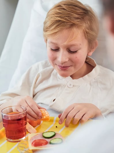 A little boy sitting in a hospital bed with a tray of food.