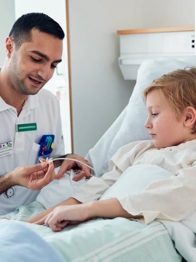 En liten pojke i en sjukhussäng undersöks av en sjuksköterska.