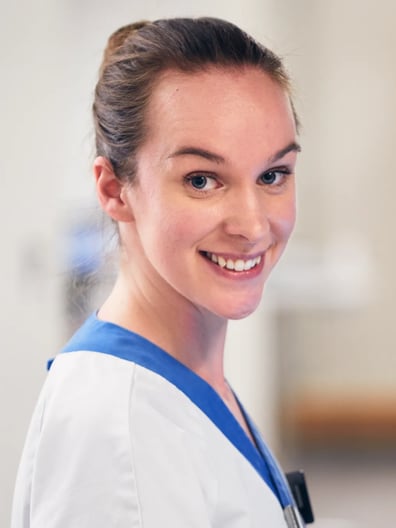 En kvinna i vårdkläder ler mot kameran.