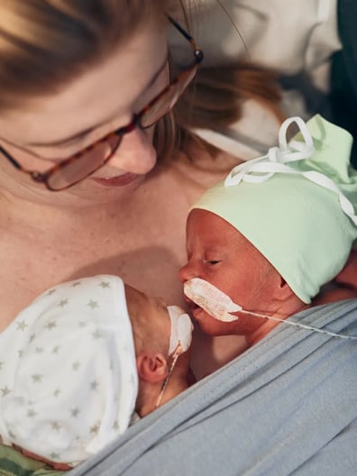 En nybliven mamma håller i sina två nyfödda tvillingar.
