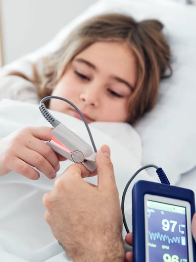 En liten flicka i en sjukhussäng blir undersökt av en sjuksköterska.