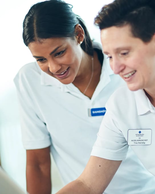 Två kvinnor i vita skjortor tittar på en surfplatta.