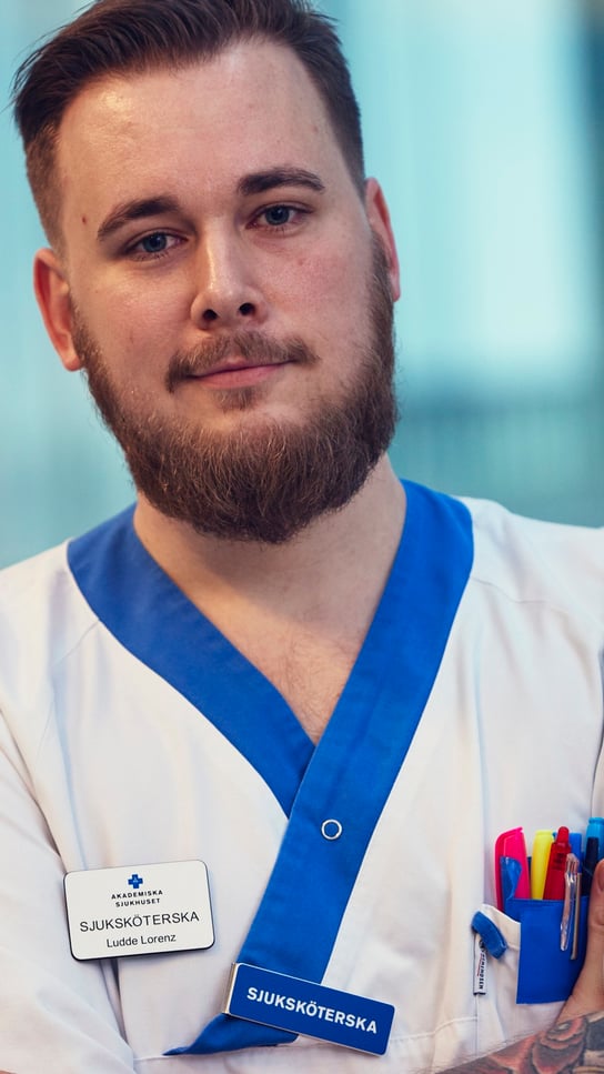 En man med skägg och tatueringar som bär en vit rock.