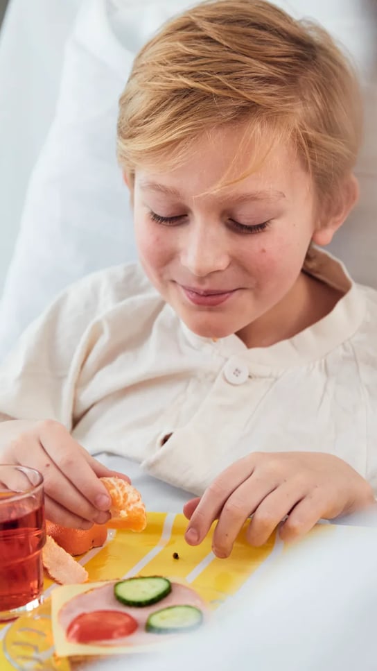 A boy is sitting in a hospital bed with a tray of food.